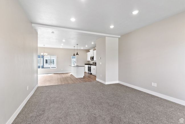 Unfurnished living room with carpet flooring, a chandelier, baseboards, recessed lighting, and a sink | Image 6