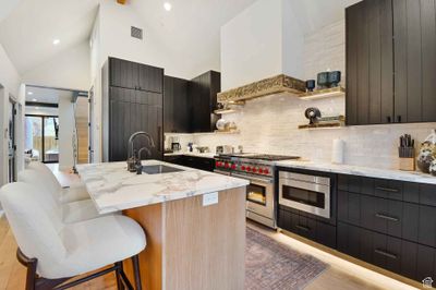 Kitchen with appliances with stainless steel finishes, custom exhaust hood, high vaulted ceiling, a breakfast bar, and a center island with sink | Image 3