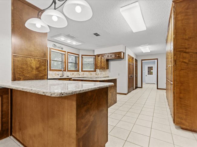 Kitchen featuring a peninsula, light tile patterned floors, a textured ceiling, tasteful backsplash, and a sink | Image 15