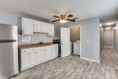 Kitchen featuring decorative backsplash, light hardwood / wood-style flooring, sink, stainless steel fridge, and white cabinetry | Image 2