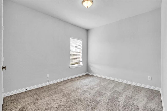 This is a bright, unfurnished room with neutral gray walls and carpet flooring. It features a single window allowing natural light and a ceiling light fixture, offering a clean slate for customization. | Image 20