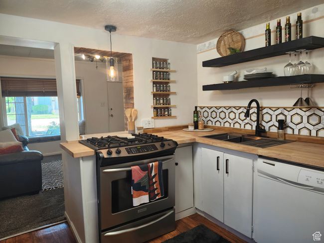 Kitchen featuring butcher block counters, dishwasher, stainless steel gas range, floating shelves, and built-in spice rack | Image 5