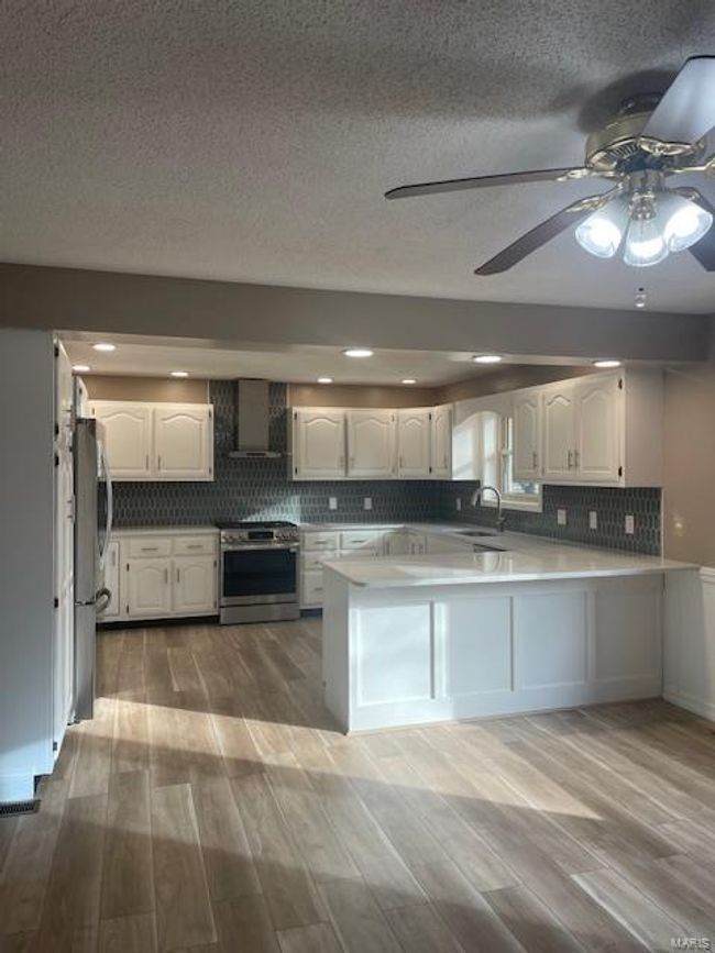 Kitchen with white cabinetry, stainless steel appliances, kitchen peninsula, and wall chimney exhaust hood | Image 14