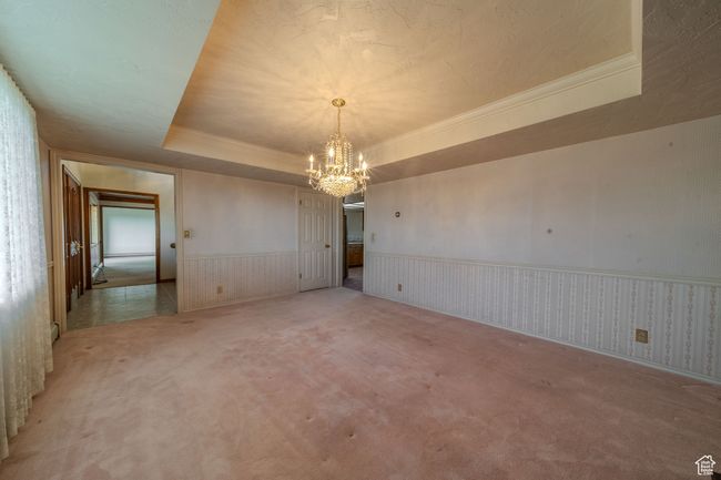 Formal dining room with crown molding, wainscoting, light carpet, a tray ceiling, and a notable chandelier | Image 12