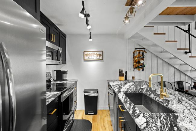 Kitchen featuring stainless steel appliances, a sink, dark cabinetry, light wood-style flooring, and light stone countertops | Image 6