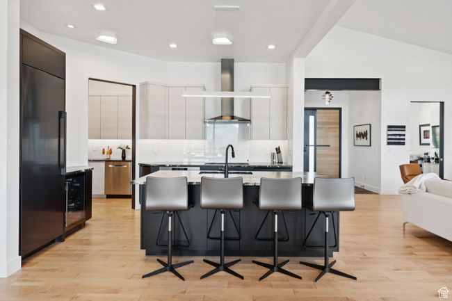 Kitchen with wall chimney exhaust hood, modern cabinets, wine cooler, light wood-type flooring, and recessed lighting | Image 15