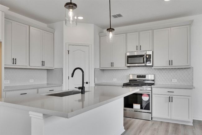 Kitchen with stainless steel appliances, light countertops, pendant lighting, tasteful backsplash, and light wood-style flooring | Image 4