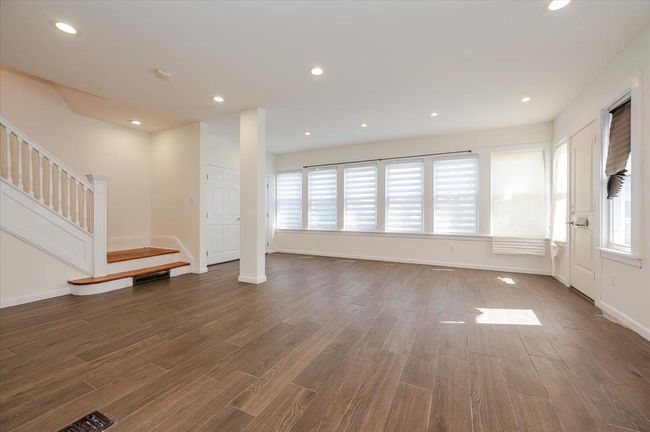 Unfurnished living room featuring a wealth of natural light, stairway, wood finished floors, and baseboards | Image 4