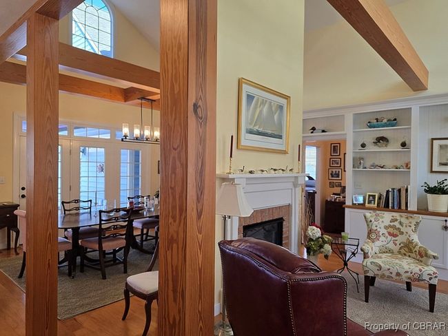 Living area with wood finished floors, an inviting chandelier, built in shelves, a glass covered fireplace, and high vaulted ceiling | Image 12