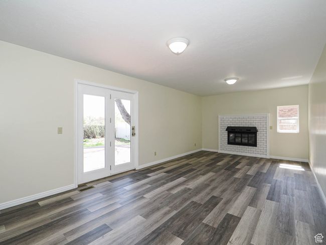 Unfurnished living room featuring plenty of natural light, dark wood-style flooring, and a brick fireplace | Image 35