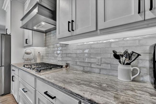 Kitchen featuring wall chimney range hood, appliances with stainless steel finishes, decorative backsplash, and light stone counters | Image 23