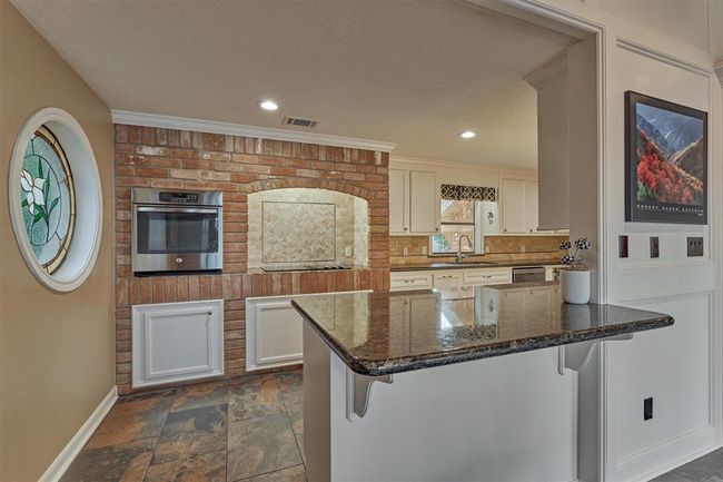 A charming stained glass window and exposed brick wall infuse the kitchen with character and warmth. The extended peninsula offers ample space for meal prep and casual seating, perfect for entertaining or everyday living. | Image 16