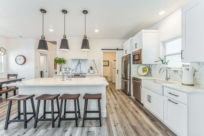 Kitchen featuring appliances with stainless steel finishes, a sink, a breakfast bar, backsplash, and gorgeous countertops. | Image 7