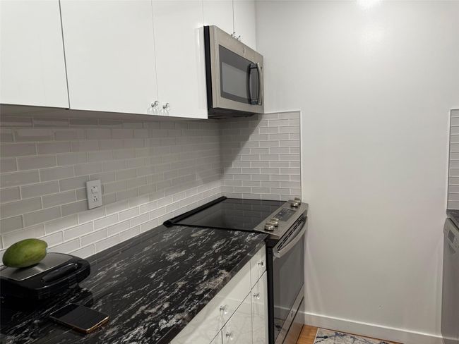 Kitchen with black / electric stove, stainless steel microwave, backsplash, white cabinets, and dark stone counters | Image 6