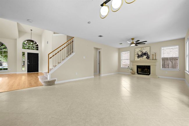 Unfurnished living room with light tile patterned floors, a ceiling fan, a glass covered fireplace, and stairway | Image 10