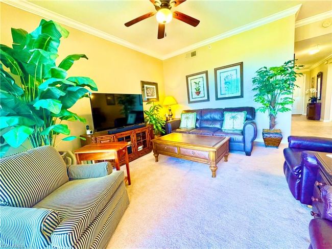 Carpeted living area featuring visible vents, crown molding, and a ceiling fan | Image 14