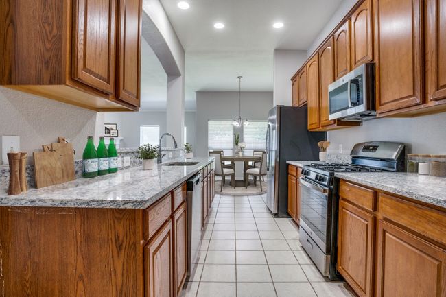 Kitchen featuring appliances with stainless steel finishes, a sink, brown cabinetry, light stone countertops, and light tile patterned floors | Image 8