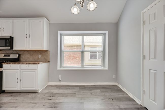 Kitchen with appliances with stainless steel finishes, white cabinets, decorative backsplash, light wood-style flooring, and a chandelier | Image 6