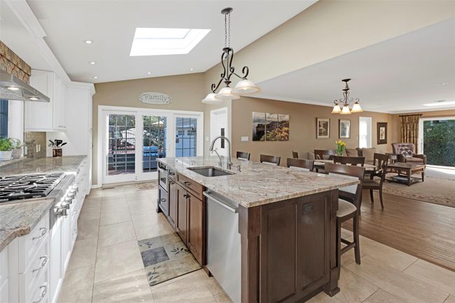 Kitchen with dishwasher, vaulted ceiling with skylight, white cabinetry, a sink, and a kitchen breakfast bar | Image 9