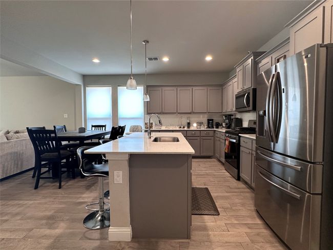 Kitchen featuring appliances with stainless steel finishes, gray cabinets, light wood finished floors, a center island with sink, and decorative light fixtures | Image 4