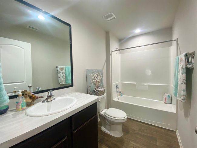 This is a bright, modern bathroom featuring a large mirror, a vanity with ample counter space, a bathtub with shower, and wood-style flooring. | Image 8