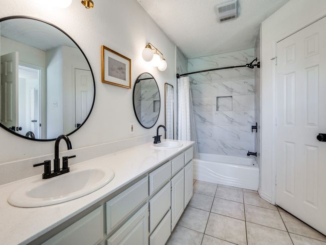 Bathroom featuring double vanity, shower / tub combo with curtain, a textured ceiling, and tile patterned flooring | Image 17