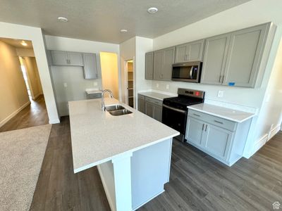 Kitchen featuring an island with sink, dark hardwood / wood-style floors, light stone countertops, stove, and sink | Image 2