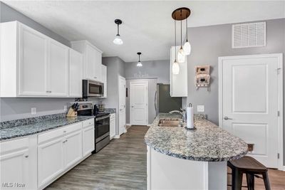 Kitchen with dark hardwood / wood-style floors, stainless steel appliances, white cabinets, sink, and hanging light fixtures | Image 2