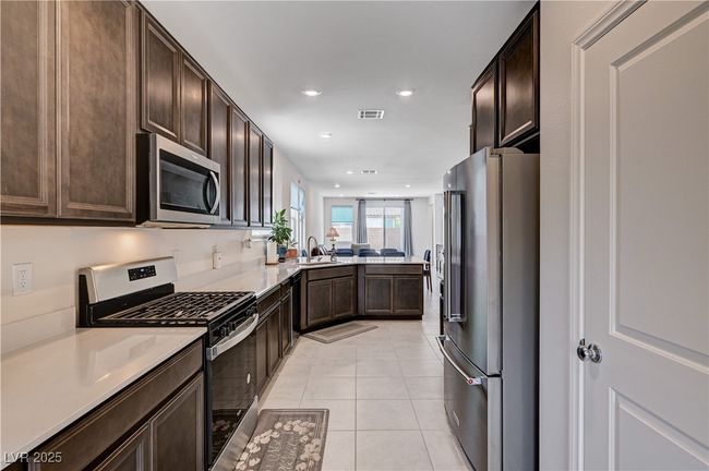 Kitchen with appliances with stainless steel finishes, dark brown cabinets, light tile patterned flooring, light countertops, and recessed lighting | Image 15