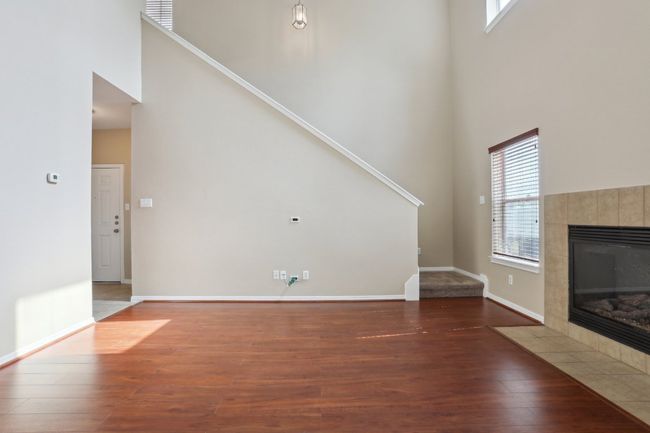Unfurnished living room with stairway, baseboards, wood finished floors, a tiled fireplace, and a high ceiling | Image 8