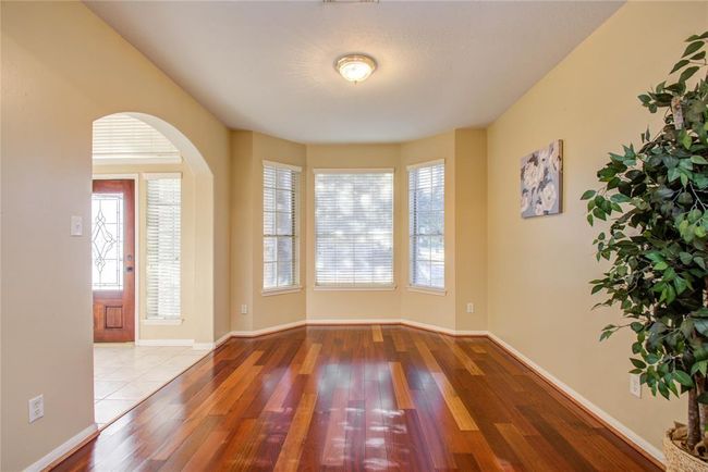 Bright, welcoming entryway with rich hardwood floors, neutral walls, and large windows. Features a decorative front door with glass panels and ample natural light. | Image 8