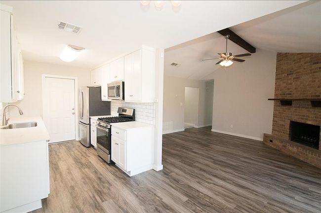 Kitchen featuring appliances with stainless steel finishes, open floor plan, wood finished floors, light countertops, and tasteful backsplash | Image 7