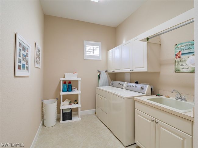 Laundry area featuring separate washer and dryer, sink, light tile flooring, and cabinets | Image 32