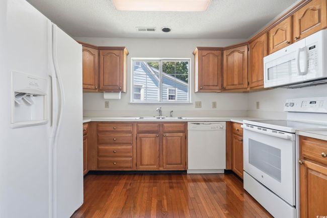 Kitchen featuring white appliances, a sink, brown cabinetry, light countertops, and dark wood finished floors | Image 15