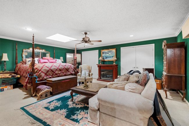 Carpeted bedroom featuring a textured ceiling, crown molding, a skylight, and a ceiling fan | Image 16
