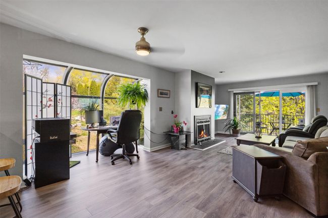 Living area with baseboards, wood finished floors, a ceiling fan, and a lit fireplace | Image 7