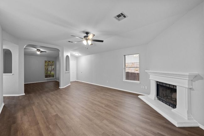Living room with a ceiling fan, natural light, arched walkways, and a fireplace with raised hearth | Image 7