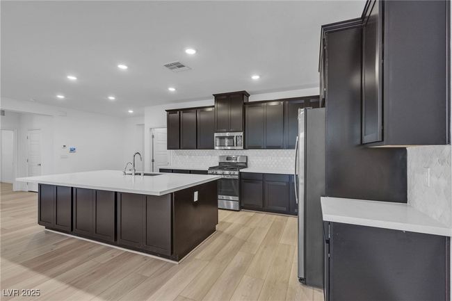 Kitchen with stainless steel appliances, a center island with sink, light wood-type flooring, decorative backsplash, and light countertops | Image 4