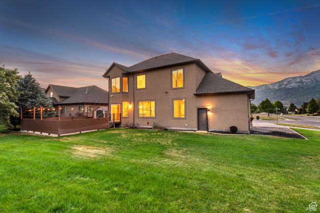 Back of house at dusk with a deck with mountain view, stucco siding, a yard, and roof with shingles | Image 40