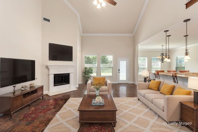 Living room featuring high vaulted ceiling, wood finished floors, ornamental molding, a fireplace with raised hearth, and a ceiling fan | Image 4