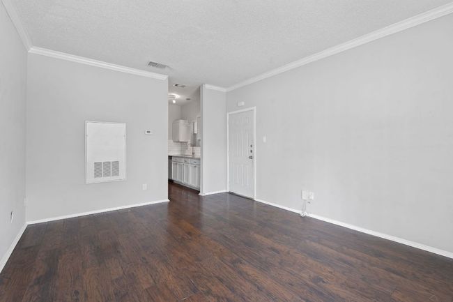 Unfurnished living room featuring dark wood-style flooring, a textured ceiling, crown molding, and visible vents | Image 5