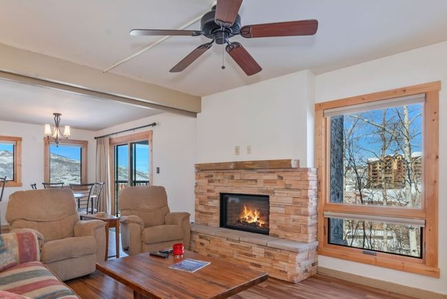 Living room with beam ceiling, a stone fireplace, wood finished floors, and ceiling fan with notable chandelier | Image 7