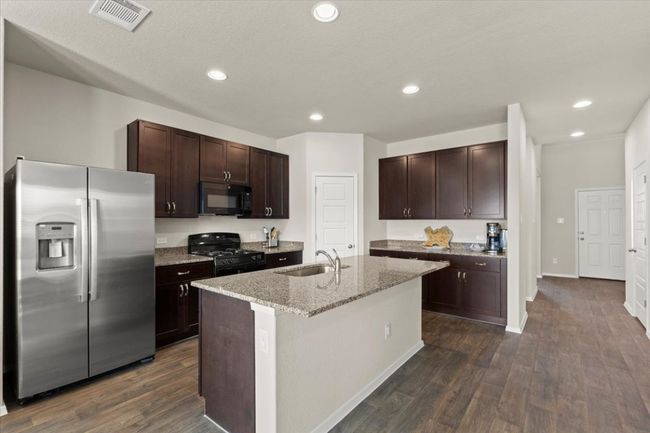 Kitchen with black appliances, a sink, dark brown cabinets, dark wood-type flooring, and recessed lighting | Image 10