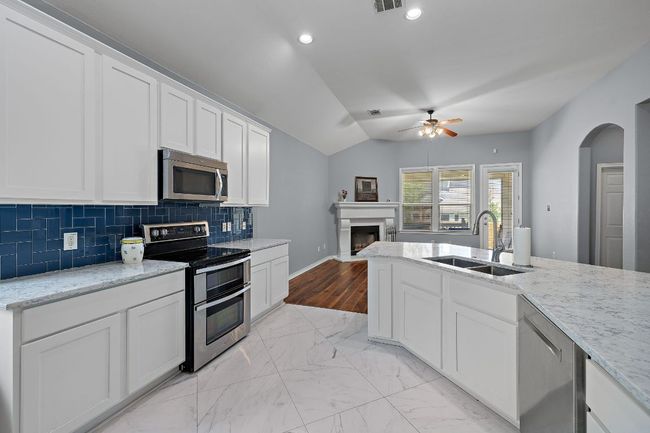 Kitchen with stainless steel appliances, a sink, a ceiling fan, a fireplace, and lofted ceiling | Image 11