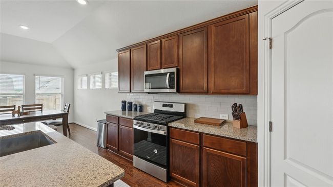 Kitchen featuring appliances with stainless steel finishes, vaulted ceiling, dark wood-type flooring, tasteful backsplash, and light stone countertops | Image 15