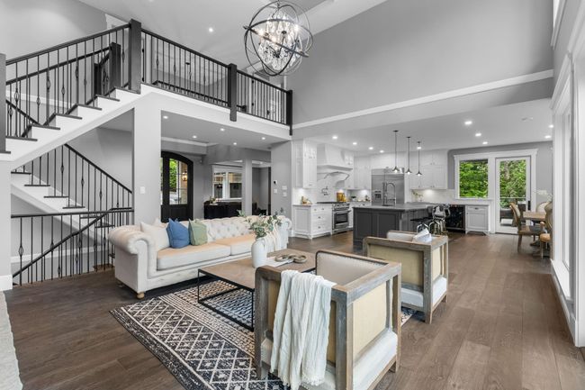 Living area with dark wood-style floors, a towering ceiling, stairway, a chandelier, and recessed lighting | Image 10