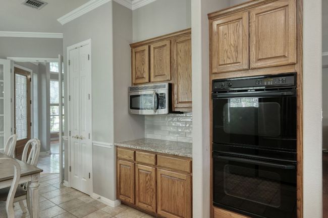 Kitchen featuring dobule oven black, crown molding, tasteful backsplash, light tile patterned floors, and stainless steel microwave | Image 12