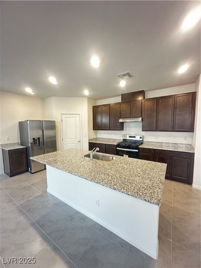 Kitchen featuring a center island with sink, visible vents, range, fridge, and a sink | Image 4