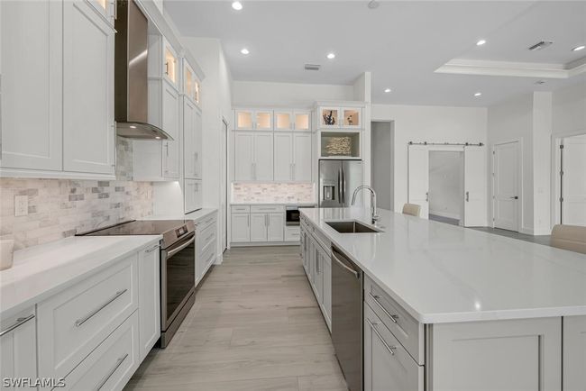 Kitchen featuring pullout spice, cookie sheet, utensil and shelving in base cabinets. Decorative lighted glass and SS designer hood. Modern Crown molding and oversized door and draw pulls. | Image 5