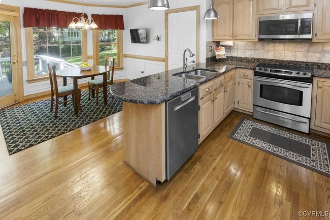 Kitchen with appliances with stainless steel finishes, a sink, wood finished floors, and a chandelier | Image 9